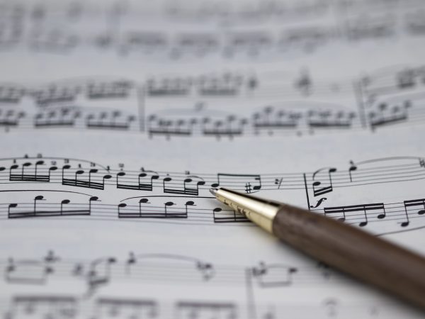 A brown pen with a gold tip laying on top of sheet music pointing to a note on the page.