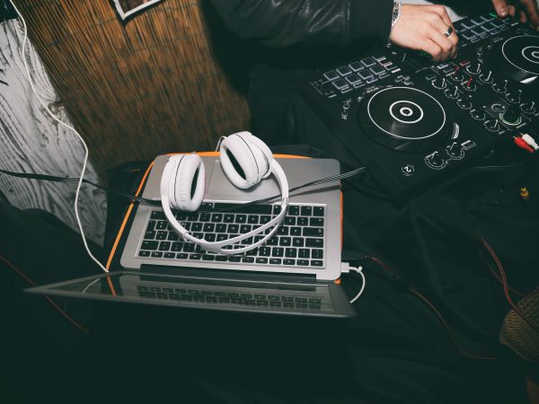 A DJ spinning on a turn table surrounded by his DJ equipment and white headphones.