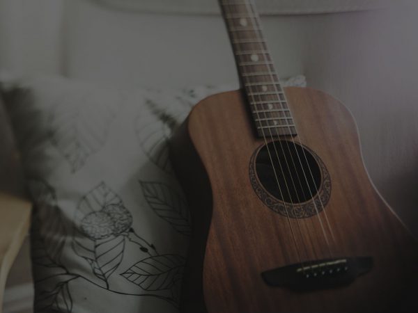 A wooden acoustic guitar standing up on a pillow.
