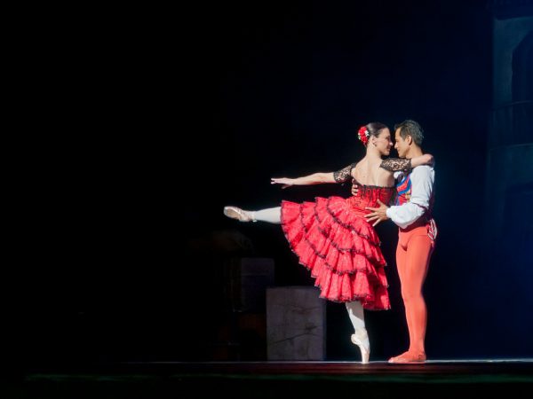 A man and woman dressed in black and red doing the tango on stage for musical theater.